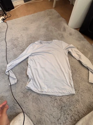 Ljusgrå långärmad topp - Säljer en ljusgrå långärmad topp i mjukt material. Enkel och stilren design med rund halsringning. Perfekt att matcha med jeans eller kjol för en clean look.