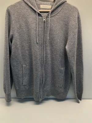 Grå hoodie med dragkedja från Sayless - Mysig grå hoodie med dragkedja framtill och två fickor. Tillverkad i mjukt stickat material och har justerbar huva med snören. Perfekt för en avslappnad och chill stil.
