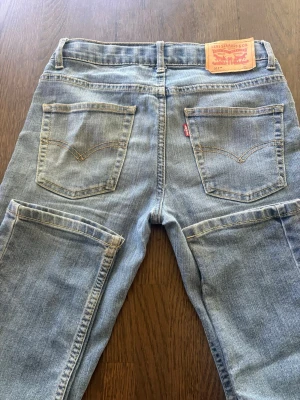 Levi's 511 Slim ljusblå jeans - Säljer ett par Levi's 511 Slim jeans i ljusblå denim. Klassisk femficksmodell med raka ben och snygga slitningar. Jeansen har Levi's ikoniska läderpatch bak och röd logotagg på fickan. Perfekta för en avslappnad och trendig look.