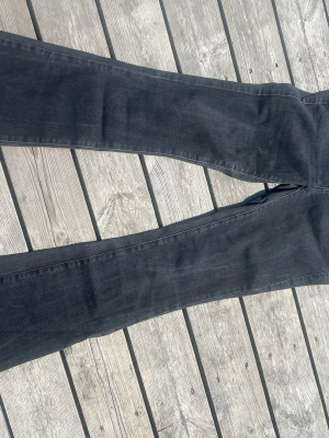Svarta bootcut jeans från Diesel, stl W26/passar 172 cm lång - Säljer ett par svarta bootcut jeans från Diesel med snygga detaljer och klassisk femficksmodell. Jeansen har en diskret tvättad look och röd textdetalj vid fickan. Perfekta för dig som gillar en tidlös och cool stil.