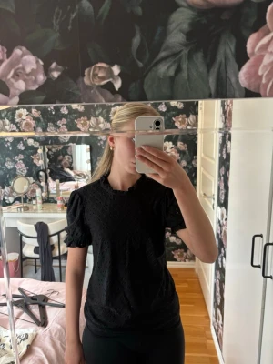 Svart topp med puffärm och broderi - Säljer en superfin svart topp med puffärmar och broderade hålmönster. Toppen har en liten volang vid halsen och är gjord i ett tunt, luftigt tyg 🌸