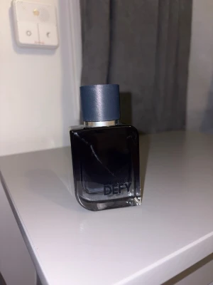 Calvin Klein Defy parfym - Säljer en Calvin Klein Defy parfym i en stilren, mörkblå glasflaska med rundade hörn och en matchande blå kork. Flaskan har en modern och maskulin design som passar perfekt på hyllan. Parfymen är känd för sin fräscha och träiga doft.