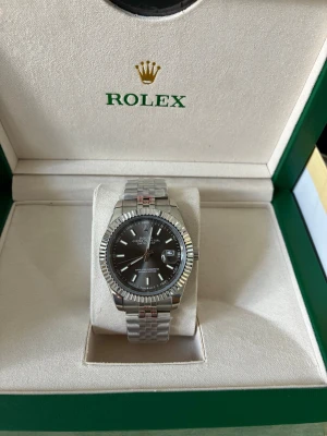 Datejust med grå urtavla  - Ny med förpackning. Urtavla 41 mm. Jubilee-armband med Oyster-spänne. Högkvalitativt automatiskt urverk med nattbelysningsfunktion. Allt som nämns i annonsen ingår. Köpt för 310 euro i juni i år. Perfekt för den som föredrar lyxiga accessoarer. 