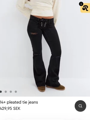 Svarta bootcut jeans med snörning - slutsolda i tall. Snygga svarta bootcut jeans med snörning i midjan och slitna detaljer vid knä och lår. Jeansen har låg midja och vida ben, vilket ger en retro vibe. Perfekta för dig som vill ha en edgy och trendig look. storlek xs i tall 