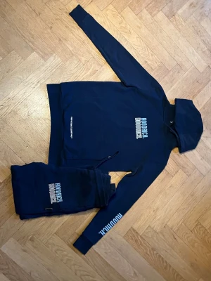 Marinblått set från Hoodrich - Snygg marinblå hoodie från Hoodrich med vit logga tryckt på bröstet och ärmen. Hoodien har huva och en klassisk känguruficka framtill. Perfekt för en avslappnad streetwear-look. Använd ett fåtal gånger och i väldigt bra skick.