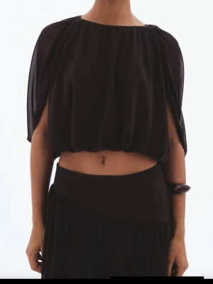 Brun croppad blus med vida ärmar - Säljer en brun croppad blus med vida, fladdriga ärmar och rund halsringning. Toppen har en luftig och flowy passform som ger en cool siluett. Perfekt för dig som vill sticka ut med en unik topp i garderoben.
