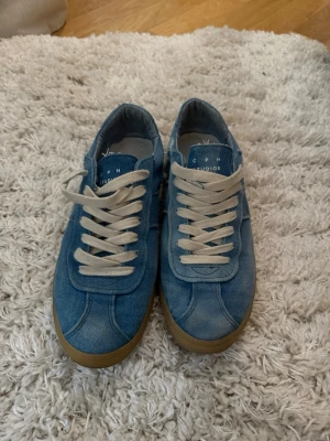 Blå denim sneakers från CPH Studios - Snygga blå sneakers från CPH Studios i denimtyg med vita skosnören och ljusbrun sula. Klassisk låg modell som passar perfekt till jeans eller shorts. Tidlös design med tydlig logga på plösen.