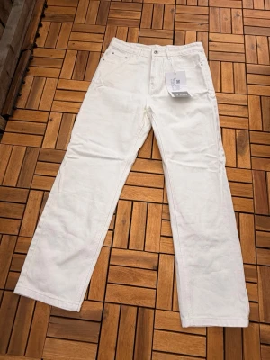 Vita raka jeans med hög midja - Säljer ett par vita jeans med rak passform och hög midja. Jeansen har klassisk femficksdesign och stängs med knapp och dragkedja. Materialet är kraftig denim i bomull som ger en clean och fräsch look.