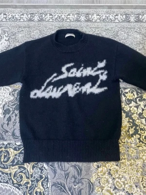 Svart stickad Saint Laurent-tröja - Den kända ysl tröjan för fem gånger mindre pengar. Detta är ett måste i din garderob för både stil och komfort. Tröjan har fantastisk kvalitet för sitt låga pris, och jag köpte den från en privat agent för nästan dubbla priset. Först till kvarn!! 🔥🫡  Priset kan diskuteras, men endast med seriösa köpare.