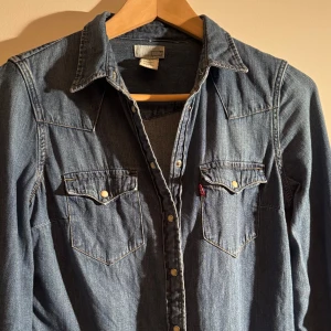 Jeansskjorta  - Säljer en klassisk blå jeansskjorta från Levi's med knappar och två bröstfickor.  Skjortan är i vanligt använt skick och har flera snygga detaljer vilket gör den unik på ett mer stilrent sätt! Hör gärna av dig om du har några frågor.💬😎