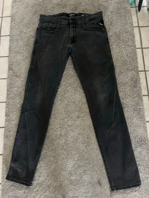 Svarta jeans från Replay - Säljer ett par svarta slim jeans från Replay med snyggt slitna detaljer och klassisk femficksdesign. Jeansen har låg midja och smal passform som sitter tajt längs benen. Perfekta för dig som gillar en modern och stilren look. Storlek: W32 L32. Aldrig använda nypris: 1200