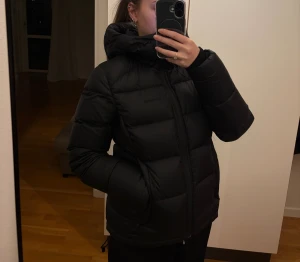 Svart pufferjacka från Everest - Säljer en svart pufferjacka från Everest med huva och dragkedja. Jackan är vadderad och har långa ärmar med tumhål för extra komfort. Perfekt för kalla dagar och har en clean, stilren look. Väldigt lite använd så i bra skick 