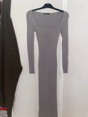 Lång ribbad klänning Gina Tricot - Supersnygg lång ribbad klänning från Gina Tricot i en beige nyans. Klänningen har lång ärm, fyrkantig ringning och figurnära passform. Perfekt för dig som gillar stilrena och enkla plagg med en modern touch.