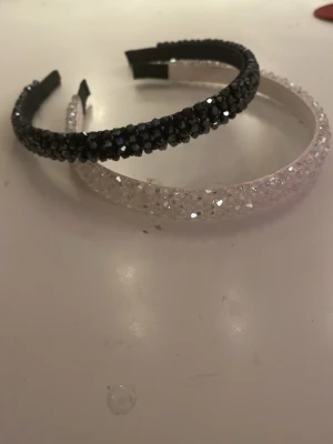 Glittriga hårband i marinblå och vitt - Två snygga hårband, ett i marinblå och ett i vitt, båda täckta med glittrande pärlor som ger en lyxig och festlig vibe. Perfekt för att lyfta din look med extra bling. Hårbanden är breda och har en stabil form som sitter bekvämt på huvudet.