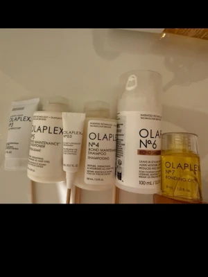 Olaplex The Full-On Shine Set kit - Utan förpackningen, endast produkter! Olaplex The Full-On Shine Set innehåller sex produkter för håret: No.3 Hair Perfector, No.4 Bond Maintenance Shampoo, No.5 Bond Maintenance Conditioner, No.6 Bond Smoother och No.7 Bonding Oil. Produkterna kommer i vita och transparenta plastflaskor och tuber med svart text och guldiga detaljer.