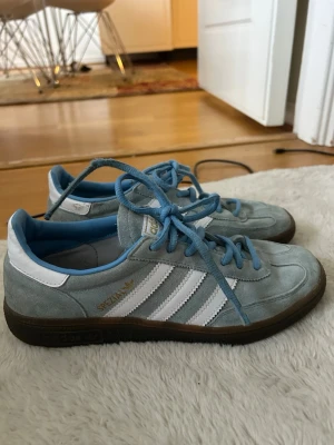 Adidas Spezial ljusblå sneakers - Säljer ett par Adidas Spezial sneakers i ljusblå mocka med vita detaljer och klassiska tre ränder på sidan. Skorna har blå snörning, vit hälkappa och gummisula. Perfekta för dig som gillar retrostil och streetwear.