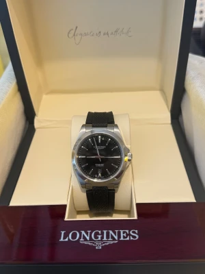 Svart Longines Conquest automatisk klocka - Säljer en stilren Longines Conquest Automatic med svart urtavla och datumvisning. Klockan har ett robust boett i rostfritt stål och svart gummiband med snygg struktur. Perfekt för dig som gillar klassisk men sportig look. Levereras i originalbox.