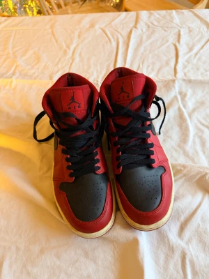 Nike Air Jordan 1 High röd/svart - Säljer ett par klassiska Nike Air Jordan 1 High i rött och svart skinn med svarta snören och vit sula. Ikonisk Jordan-logga på sidan och tungan. Perfekta för dig som vill ha en streetwear-vibe och älskar retro sneakers. Strl 41. Fint skick, nötta i tyget som som blir typ direkt - se bild. 