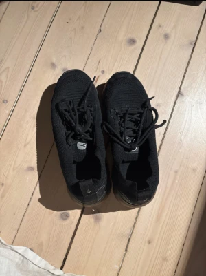 Svarta stickade sneakers  - Svarta sneakers  med stickad ovandel och snörning. Skorna har en rund tå och platt sula, vilket gör dem riktigt sköna att gå i. Perfekt för dig som gillar sportig och clean stil. 