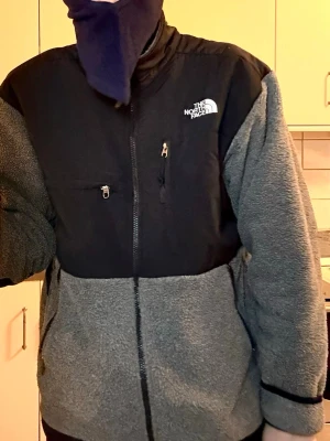  The North Face Denali Fleece - Säljer en grå och svart fleecejacka från The North Face med hög krage och hel dragkedja framtill. Jackan har två bröstfickor med dragkedja och broderad logga på både fram- och baksida. Perfekt för kyliga dagar och riktigt skön att ha på sig.