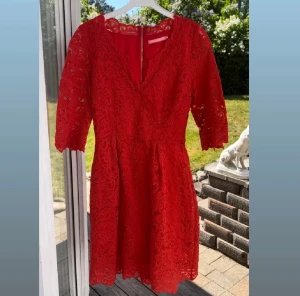 Röd spetsklänning med v-ringning - Superfin röd klänning i spets med v-ringning och halvlånga ärmar. Klänningen har dragkedja i ryggen och ett blommigt spetsmönster som ger en romantisk vibe. 