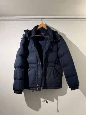 Mörkblå dunjacka Polo Ralph Lauren -  Tjena säljer en snygg mörkblå dunjacka från Polo Ralph Lauren i storlek M! Lite äldre modell som inte säljs längre. Inga defekter finns på jackan. Hör av er vid fler frågor och funderingar. Mvh