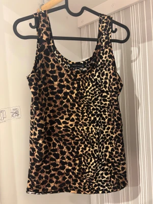 Leopardmönstrad linnetopp från Giant Basics - Säljer en snygg leopardmönstrad linnetopp från Giant Basics. Toppen är ärmlös med rund halsringning och har ett coolt djurmönster i svart och beige. Perfekt för dig som vill sticka ut med en trendig look.