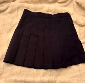 Mörkblå plisserad kjol från American Apparel - Säljer en mörkblå plisserad kortkjol från American Apparel. Kjolen har klassisk skoluniforms-vibe med breda veck, knäppning i sidan med knapp och dragkedja. Perfekt för dig som gillar stilrena och tidlösa plagg. Materialet är kraftigt och håller formen snyggt. Markerad med storlek M men är lite liten. Midjemått 36 cm *2. Därför skriver jag small här. Skicket är perfekt, 10/10