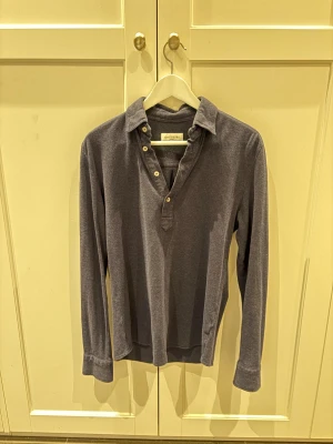 Blå henley från John Henric - Säljer en stilren blå henley från John Henric. Skjortan har lång ärm, klassisk krage och fyra knappar framtill. Tillverkad i mjuk bomull som känns skön mot huden. Perfekt för dig som gillar en avslappnad men ändå snygg look.