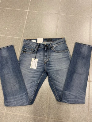 Blå tiger of Sweden  jeans W28 L34 - Snygga blå jeans från Tiger of Sweden  med klassisk femficksdesign och raka ben. Jeansen har en brun läderpatch bak i midjan och kontrastsömmar. Modellen är straight leg med smal fot, perfekt för dig som gillar tidlös stil.