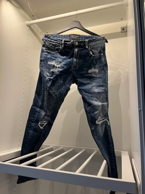 Blå slitna jeans från Supply & Demand - Snygga blå jeans med slitningar och trasiga detaljer från Supply & Demand. Modellen är smal med normal passform och har klassisk femficksdesign. Perfekt för dig som gillar en edgy streetstil och vill sticka ut med coola jeans.