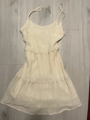 Ljusbeige sommarklänning med tunna axelband - Supersöt ljusbeige kort klänning från H&M med tunna axelband och lätt rynkad struktur. Klänningen har en volangig kjol och  en underkjol för extra komfort. Perfekt för varma dagar och har en luftig känsla.