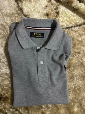 Grå piké från Polo Ralph Lauren - Säljer en stilren grå pikétröja från Polo Ralph Lauren med klassisk krage och två knappar framtill. Pris kan alltid diskuteras bara att skriva till mig över funderingar!