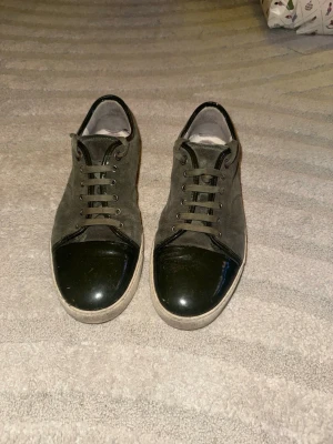 Gröna sneakers från Lanvin i mocka - Snygga gröna sneakers från Lanvin med ovandel i mocka och lackade detaljer på tån och runt öppningen. Skorna har snörning och en platt, vit sula. Perfekt för dig som gillar en clean men ändå unik look.