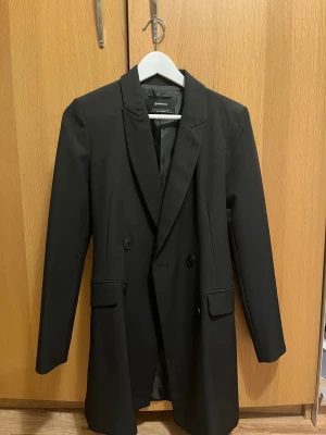Svart kavaj från Stradivarius XS - Snygg svart kavaj från Stradivarius i storlek XS. Dubbelknäppt modell med klassisk krage, långa ärmar och fickdetaljer framtill. Tillverkad i ett slätt tyg med fodrad insida, perfekt för en stilren look.