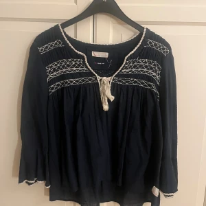 Mörkblå blus Odd Molly med broderi - Säljer en mörkblå blus från Odd Molly med vita broderade detaljer och knyt framtill. Blusen har lång ärm, v-ringad hals. Använd men bra skick fortfarande. Osäker vad storlek 1 betyder men skulle gissa på en S-M
