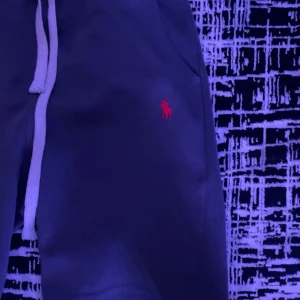 Mörkblå shorts från Polo Ralph Lauren - Snygga mörkblå shorts från Polo Ralph Lauren med klassisk röd logga broderad på benet. De har vit snörning i midjan och är tillverkade i mjukt bomullsmaterial, perfekta för chill dagar. Passformen är normal och stilen är enkel men stilren.