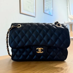 Svart quiltad väska - Snygg svart trendig axelväska med guldfärgade detaljer. Väskan är tillverkad i skinn och har det ikoniska CC-spännet framtill. Insidan är vinröd och har praktiska fack. Perfekt för dig som vill ha en lyxig och tidlös look. Använd vid ett tillfälle så nyskick och väl omhändertagen🩷