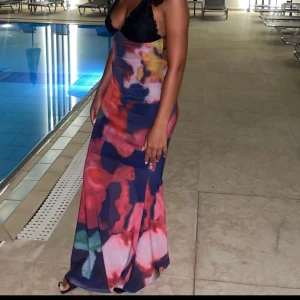 Färgstark långklänning med mönster - Säljer en maxiklänning med färgstarkt abstrakt mönster i blått, rött, rosa och grönt. Klänningen har smala axelband och är ärmlös med en figurnära passform. Perfekt för dig som vill sticka ut med en unik look och älskar färg.