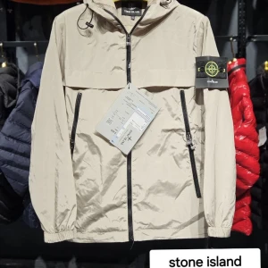 Stone Island vindjacka med huva - Snygg vindjacka från Stone Island med ikonisk patch på ärmen, dragkedja framtill och två snedställda fickor med dragkedja. Jackan har justerbar huva och elastiska muddar. Finns i beige, blå, grå och grön. Perfekt för dig som vill ha en clean och sportig look. S m l xl xxl