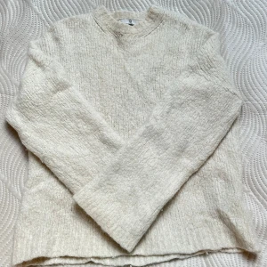 Vit stickad tröja med rund hals - Mysig vit stickad tröja med rund hals och långärmad design. Tröjan ribbade detaljer vid hals och nederkant. Märke Wakakuu Icons 