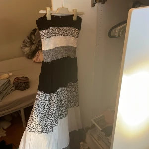 Långklänning i svartvitt med mönster - Säljer en långklänning i svart och vitt med flera olika mönster. Klänningen har breda block i blommigt, randigt och enfärgat tyg. Den är ärmlös och har en luftig, flowy passform som känns riktigt chill och somrig.