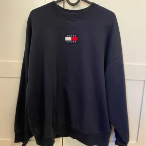 Mörkblå sweatshirt från Tommy Jeans - Säljer en mörkblå sweatshirt från Tommy Jeans med klassisk logga broderad på bröstet. Tröjan har rund halsringning, ribbade muddar och en loose passform. Perfekt för dig som gillar stilren och enkel streetwear.