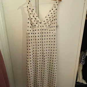 Vit prickig långklänning från H&M - Supersnygg långklänning från H&M i vit satinlook med svarta prickar. Djup v-ringning och smala axelband ger en stilren och trendig vibe. Klänningen har en flowy passform och är perfekt för dig som gillar ett klassiskt men ändå lekfullt mönster.