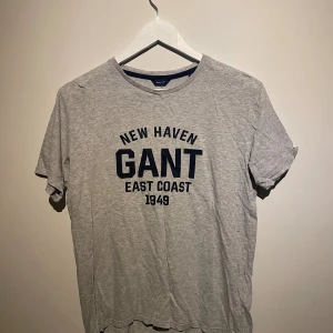 Grå GANT t-shirt med tryck - Snygg grå t-shirt från GANT med mörkblå tryck 'NEW HAVEN GANT EAST COAST 1949' på bröstet. Klassisk rund hals och korta ärmar. Bomull! 
