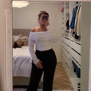 Vit offshoulder topp med pärlor - Säljer en vit offshoulder topp med långa ärmar och snygga pärldetaljer över axelpartiet. Toppen har en draperad design upptill som ger en cool och elegant vibe. Perfekt för dig som vill sticka ut med en unik och trendig look.