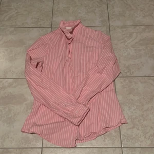 Rosa randig skjorta med knappar - Snygg rosa skjorta med vita ränder och klassisk krage. Oklart vilket märke och storlek, skulle tippa på H&M och XS-S. Köpt second hand. 