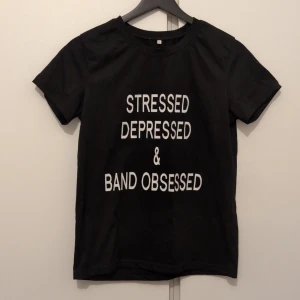 Svart t-shirt med tryck - Svart t-shirt i bomull med vit text på framsidan: 'STRESSED DEPRESSED & BAND OBSESSED'. Klassisk rund hals och korta ärmar. Perfekt för dig som älskar band och vill visa din personlighet med ett statement-plagg. Står storlek M men tror mer att den är som S.