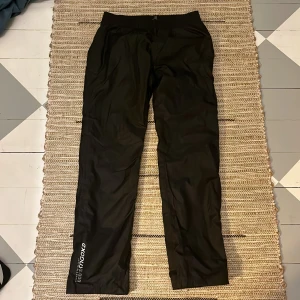 Svarta täckbyxor från McKinley strl 38 - Svarta täckbyxor från McKinley i storlek 38. Byxorna har resår i midjan, justerbara benslut med kardborre och tryckt logga på benet. Perfekta för vinterns alla äventyr och håller dig torr och varm. Snygg och enkel design som funkar till allt.
