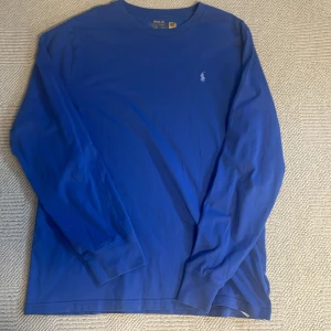 Blå långärmad tröja Polo Ralph Lauren - Snygg blå långärmad tröja från Polo Ralph Lauren i storlek XL. Tröjan är i mjuk bomull och har en klassisk rund hals samt den ikoniska broderade loggan på bröstet. Perfekt för dig som gillar stilrena och tidlösa plagg.